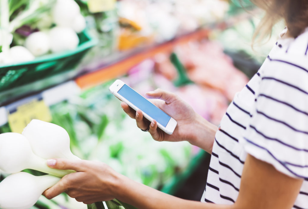 alt="woman on mobile phone in store by produce"