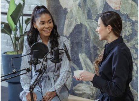 alt=women-talking-by-microphone-podcast