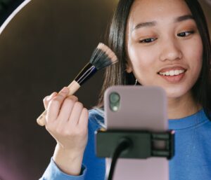 alt=woman-putting-on-makeup-in-front-of-phone